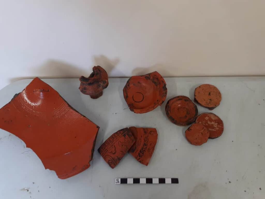 Selection of ceramic finds from the dump deposits below the Roman building, including a stamped Samian ware dish, an unguent bottle and four gaming counters made from pot bases